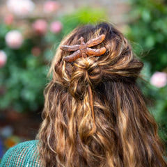 Close-up of a person's hair with a decorative hair clip against a blurred natural background