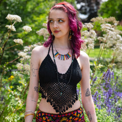 Woman with pink hair and tattoos standing in a garden with flowers and greenery.