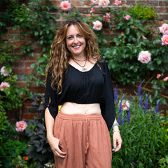 Woman standing in a garden with flowers and a brick wall in the background
