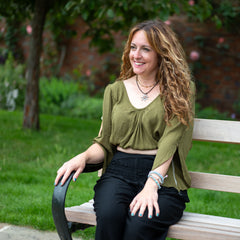 Woman sitting on a bench in a park with greenery and a tree in the background