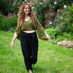 Woman in green top and black pants standing in a garden with flowers and greenery.
