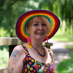 Person wearing a colorful rainbow hat and dress with a blurred green background