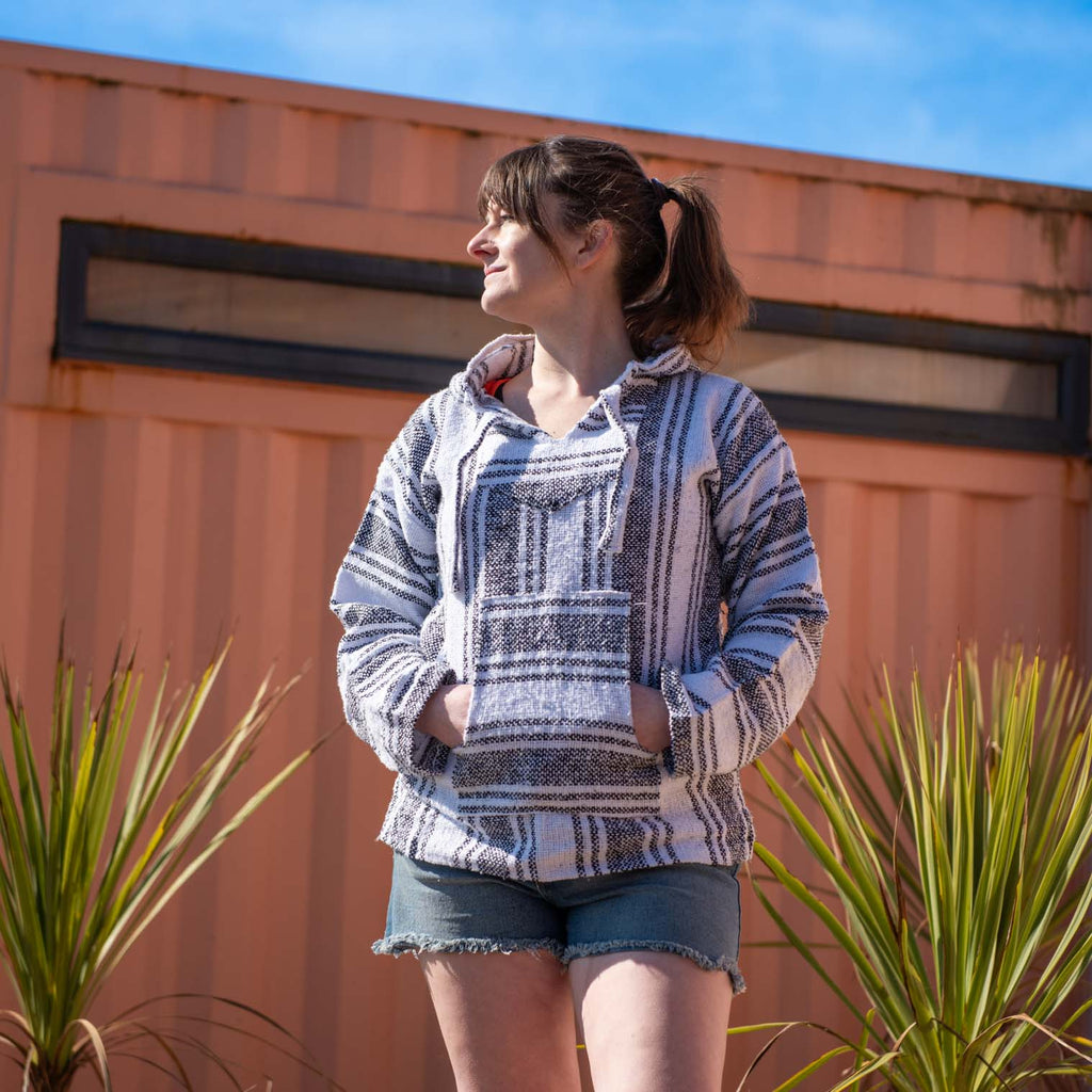 A woman wearing a white natural Baja Hoodie on a beach on a sunny day.