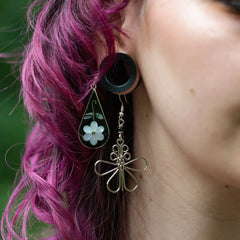 Close-up of a person wearing earrings with floral designs, one green and one silver.