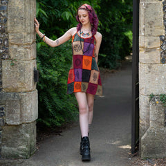 Woman in a colorful patchwork dress standing in a stone archway with greenery.