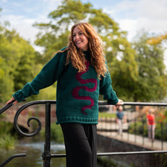 Woman wearing a green sweater with a pink design, standing outdoors by a railing.