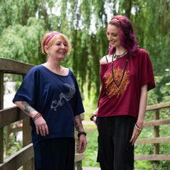 Two women standing on a wooden bridge with greenery in the background