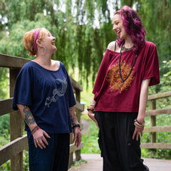 Two women with vibrant hair colors standing on a wooden bridge in a green, natural setting.