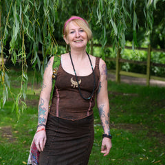 Woman in a brown outfit standing under a tree with greenery around