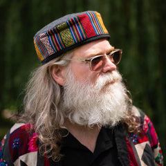 Man with a colorful hat and sunglasses looking to the side with a blurred green background