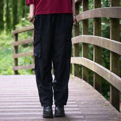 Person wearing black cargo pants standing on a wooden bridge with greenery in the background