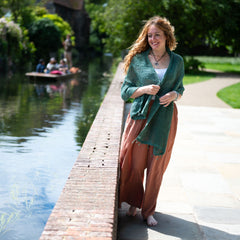 Woman standing on a wooden path by a canal with greenery and people in the background
