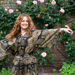 Woman in a patterned dress standing in front of a brick wall with greenery and flowers.