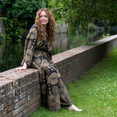 Woman in a patterned outfit sitting on a brick wall by a canal